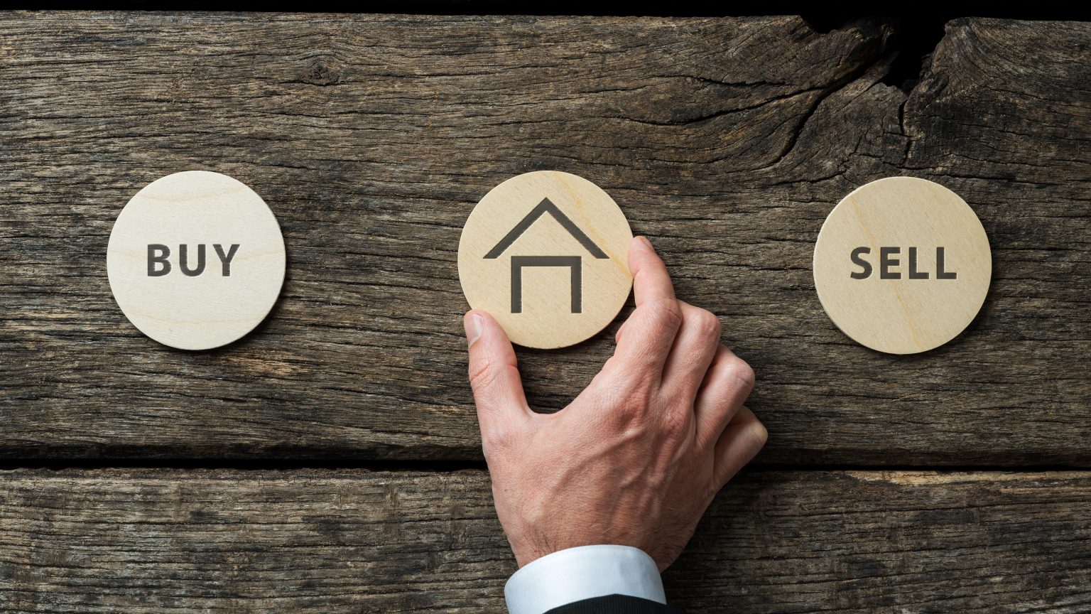 Mano eligiendo una ficha en forma de casa entre Comprar y Vender