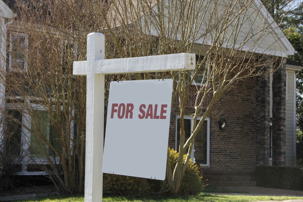 For Sale sign in front of a brick home