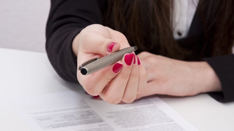 Person holding a pen over a document on a table